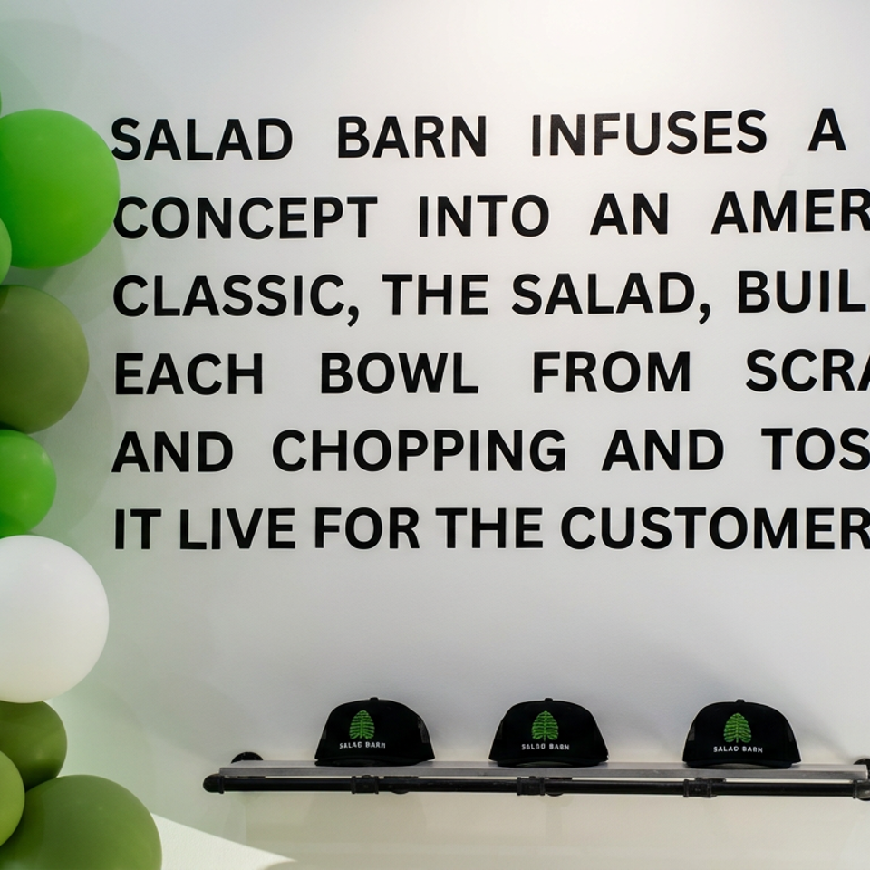 Green and white balloon installation beside a wall displaying Salad Barn’s concept statement and branded caps.